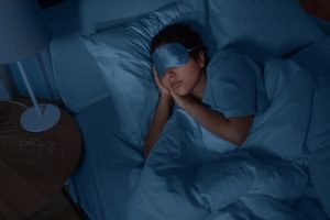 person sleeping with a sleep mask in their bed